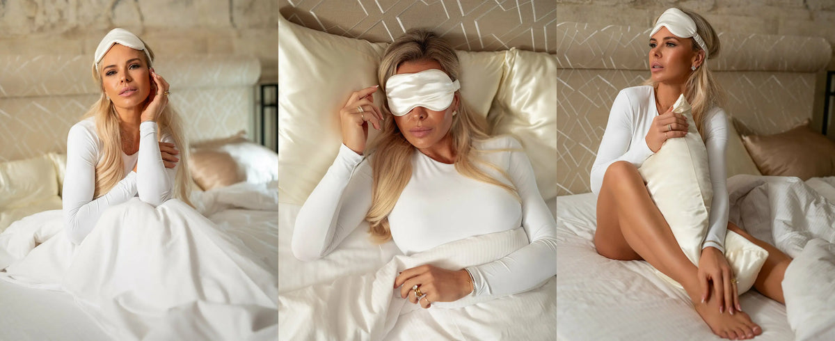 Woman in a white outfit with a pure sleep mask on, sitting on a bed.