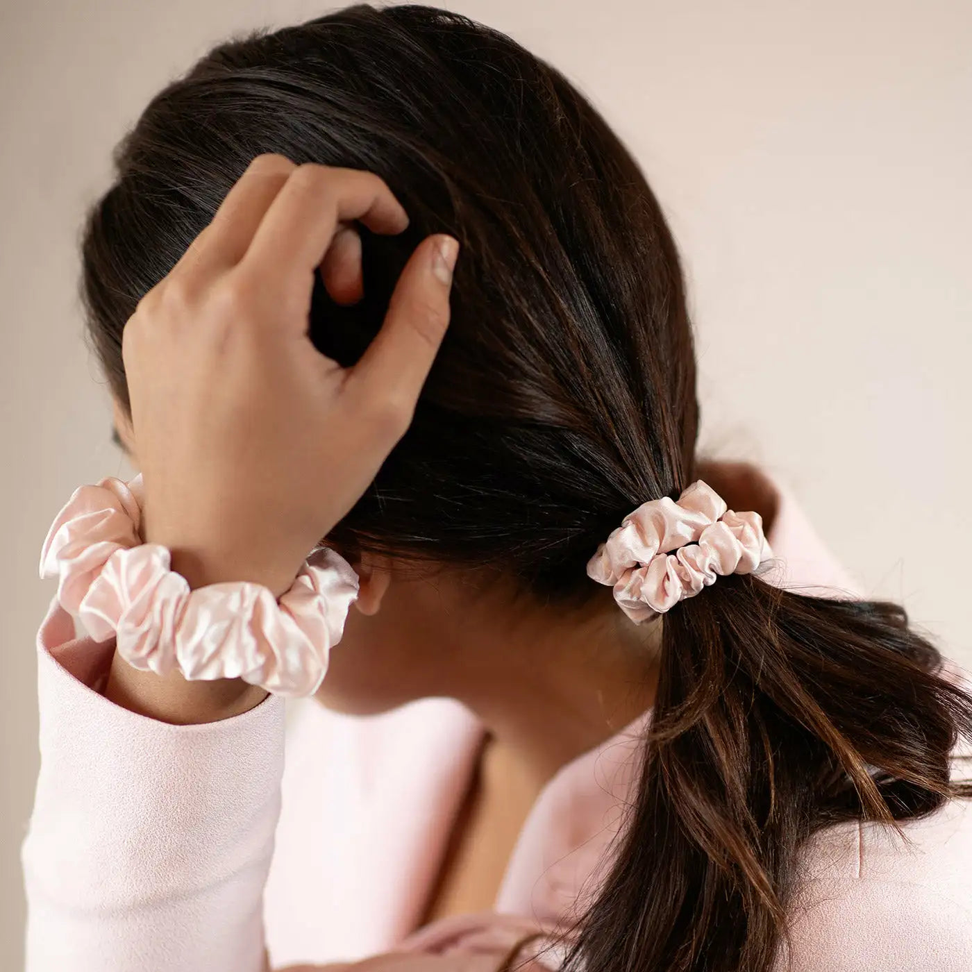 Person with a ponytail using pink scrunchies against a neutral background